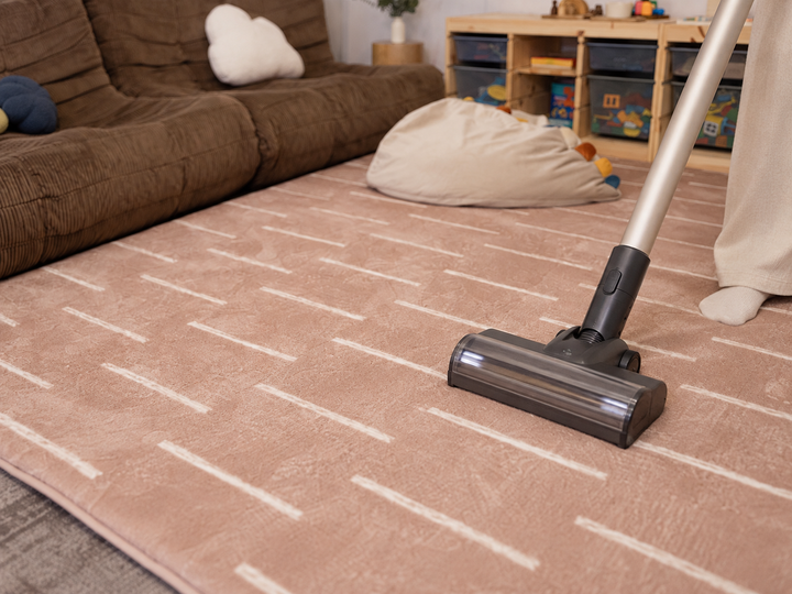 The Lollibly Shortbread Plush Playmat being vacuumed in a cosy living room, showcasing its easy-to-clean surface.