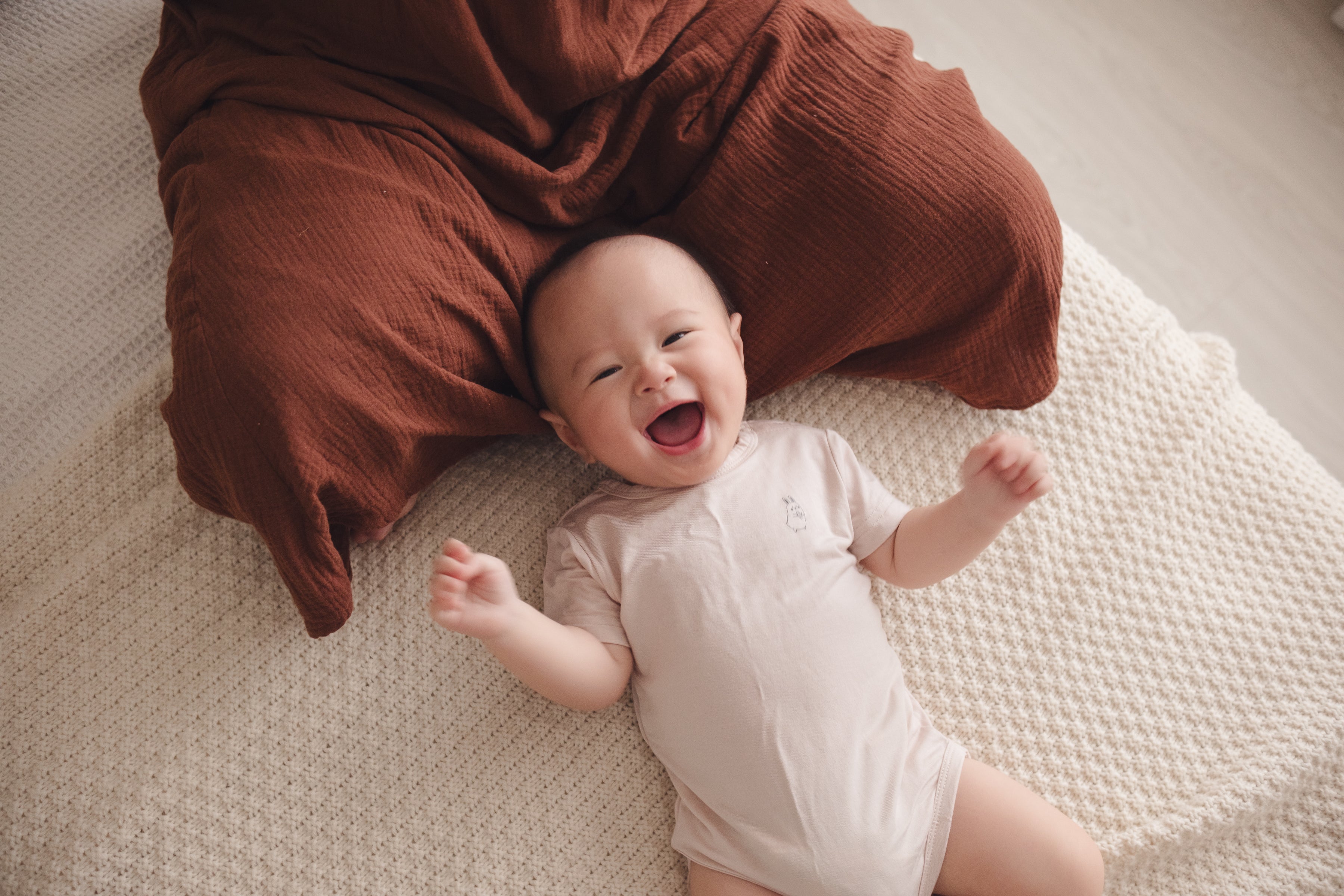 Smiling baby in a beige onesie lying on mum’s lap