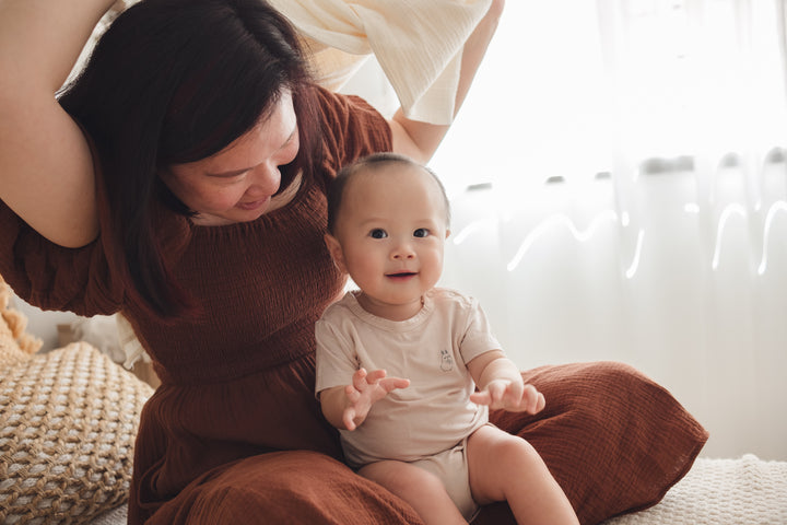 Woman holding a baby on her lap, with the baby wearing a beige onesie