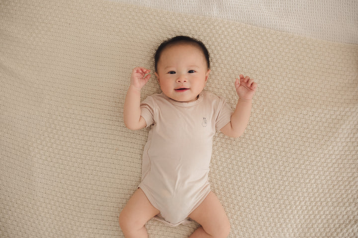 Baby lying comfortably on a bed, wearing a beige onesie