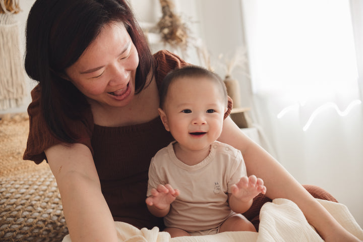 Woman cradling a baby on her lap while the baby wears a beige onesie
