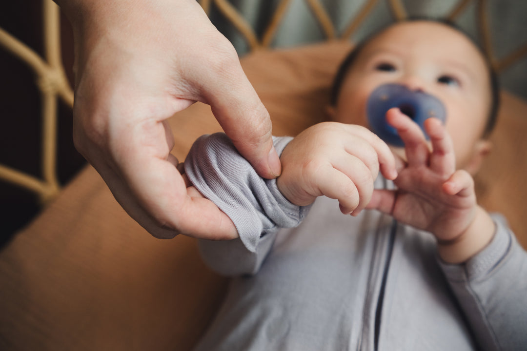 Baby lying in a cot while an adult flips over the sleep suit hand mitten