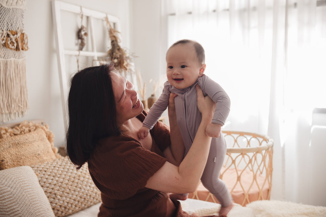 Smiling woman cuddling a baby in a cosy bedroom, with the baby dressed in a lavender sleepsuit