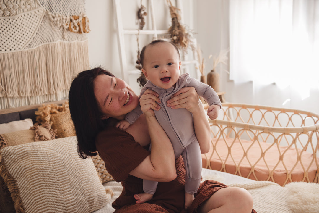 Woman holding up a baby wearing a lavender sleep suit 
