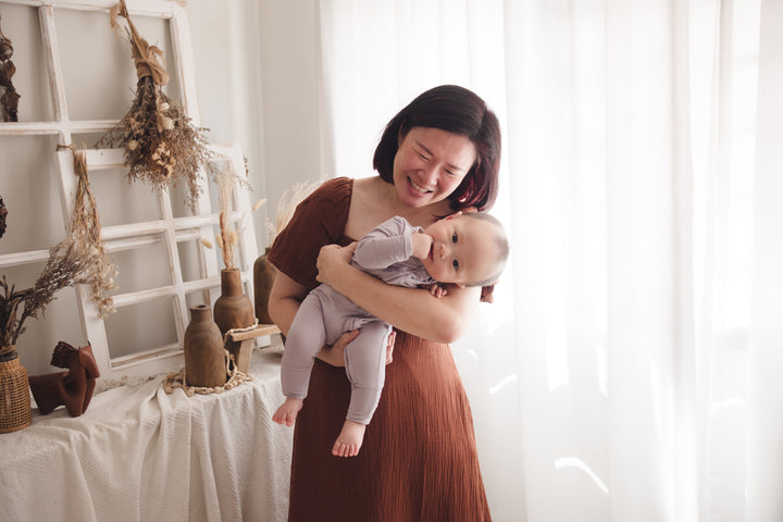 Woman holding her baby close as they tilt to one side, with the baby wearing a lavender sleep suit