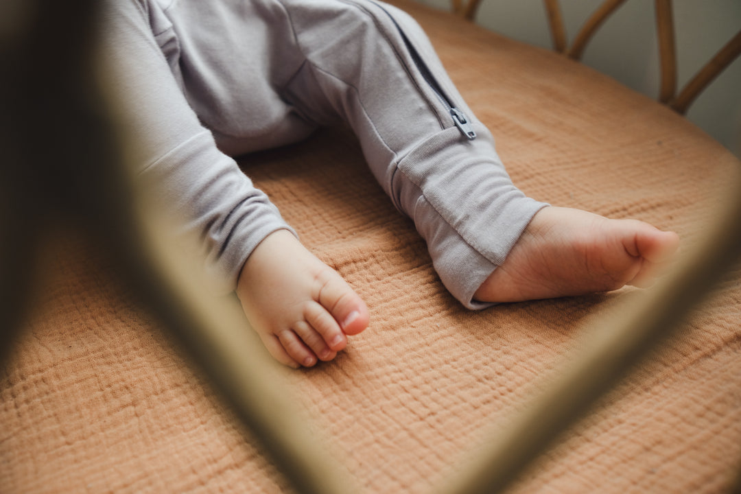 Baby lying in a crib wearing a lavender sleepsuit, showing the fold-over foot mitten detail