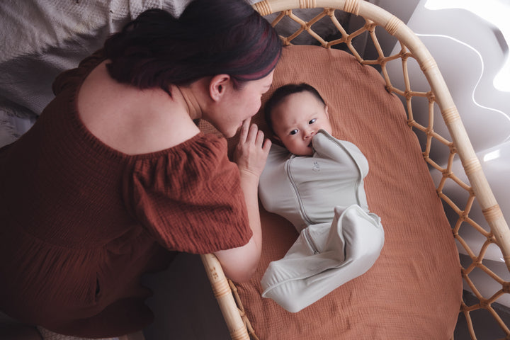 Mother leaning over the cot, looking lovingly at her baby wrapped in a swaddle bag