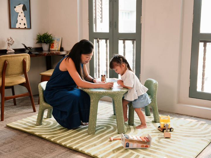 A woman and a toddler playing and colouring together at a table placed on the Lollibly Kaya Plush Playmat.
