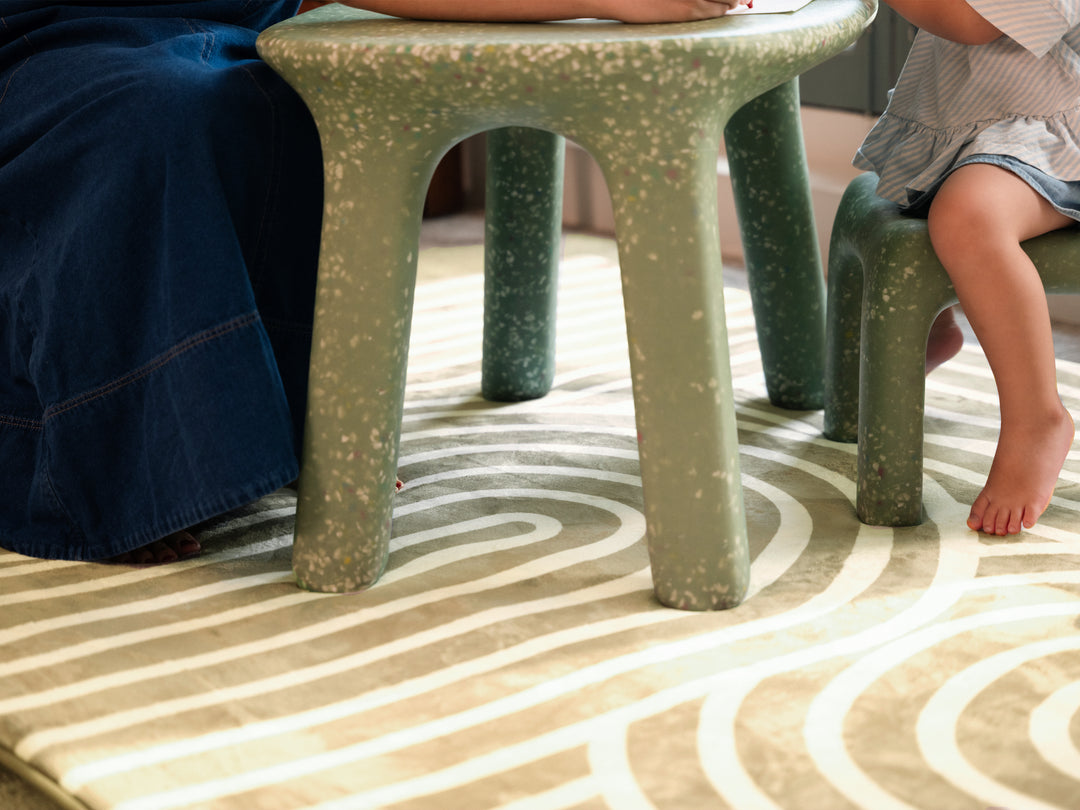 Close-up of a parent and child sitting on stools placed on the Lollibly Kaya Plush Playmat.