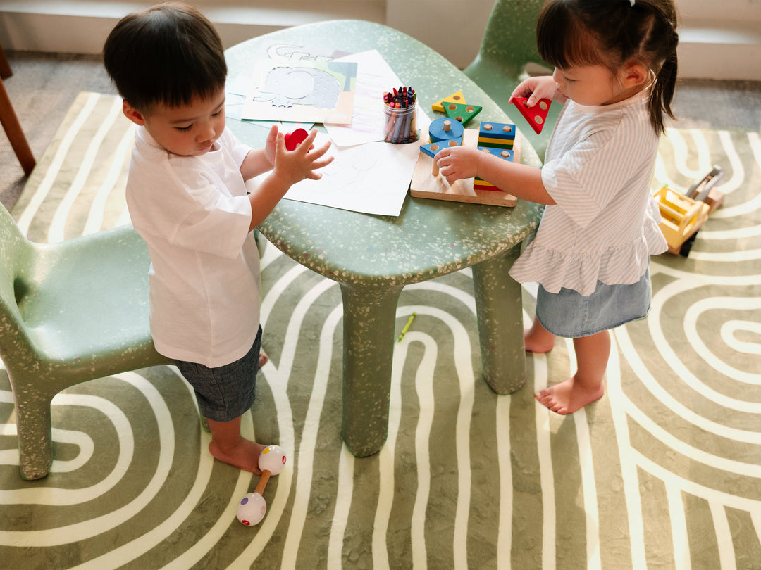 Two young children playing together at a small green speckled table placed on the Lollibly Kaya Plush Playmat.