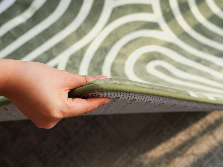 Close-up of a hand lifting the corner of the patterned Lollibly Plush Playmat to showcase its cushioned thickness.