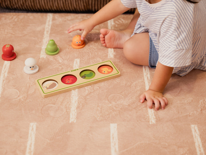 A toddler sitting on the Lollibly Shortbread Plush Playmat, featuring a patterned design, while playing with a wooden sorting toy.