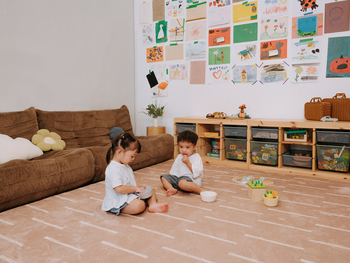 Two young children sitting and playing together on the Lollibly Shortbread Plush Playmat in a cosy living room.