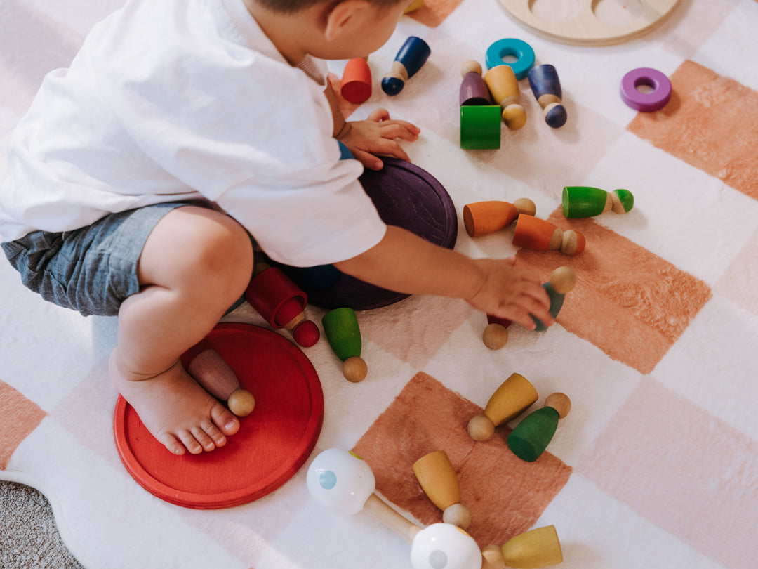 A toddler playing with colourful wooden blocks and stacking rings on the Lollibly Waffle Plush Playmat, featuring a soft checkered design.