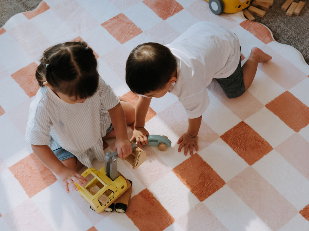 Two children playing on a large, scalloped checkered plush play mat.