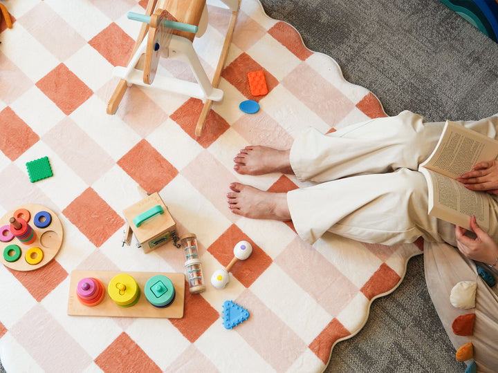 Top-down view of a person reading a book on the Lollibly Waffle Plush Playmat, featuring a two-tone checkered design and scalloped edges.