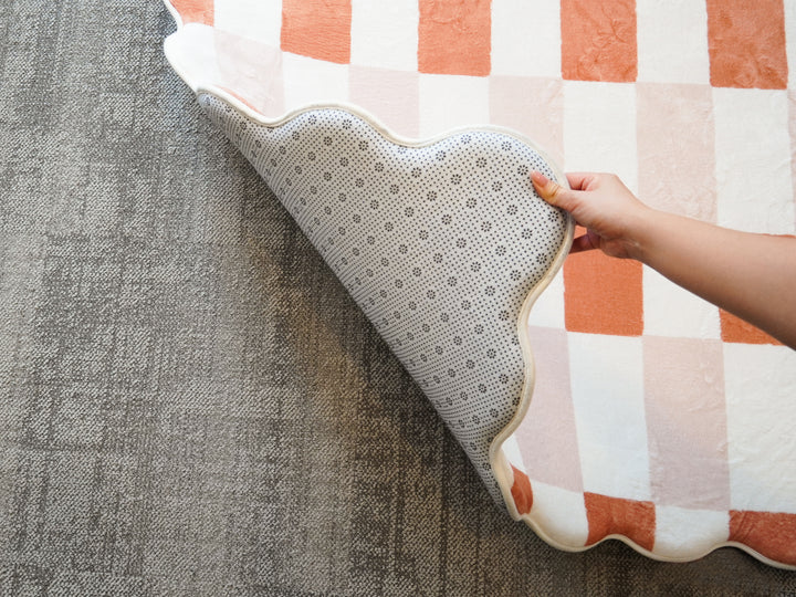 A hand lifting the corner of the Lollibly Waffle Plush Playmat to reveal its non-slip underside.